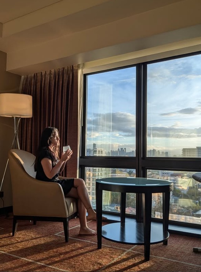 Woman reflecting by a sunlit window with city view